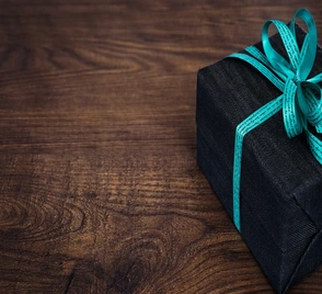 photo of a black gift box with baby blue ribbon on a wooden table